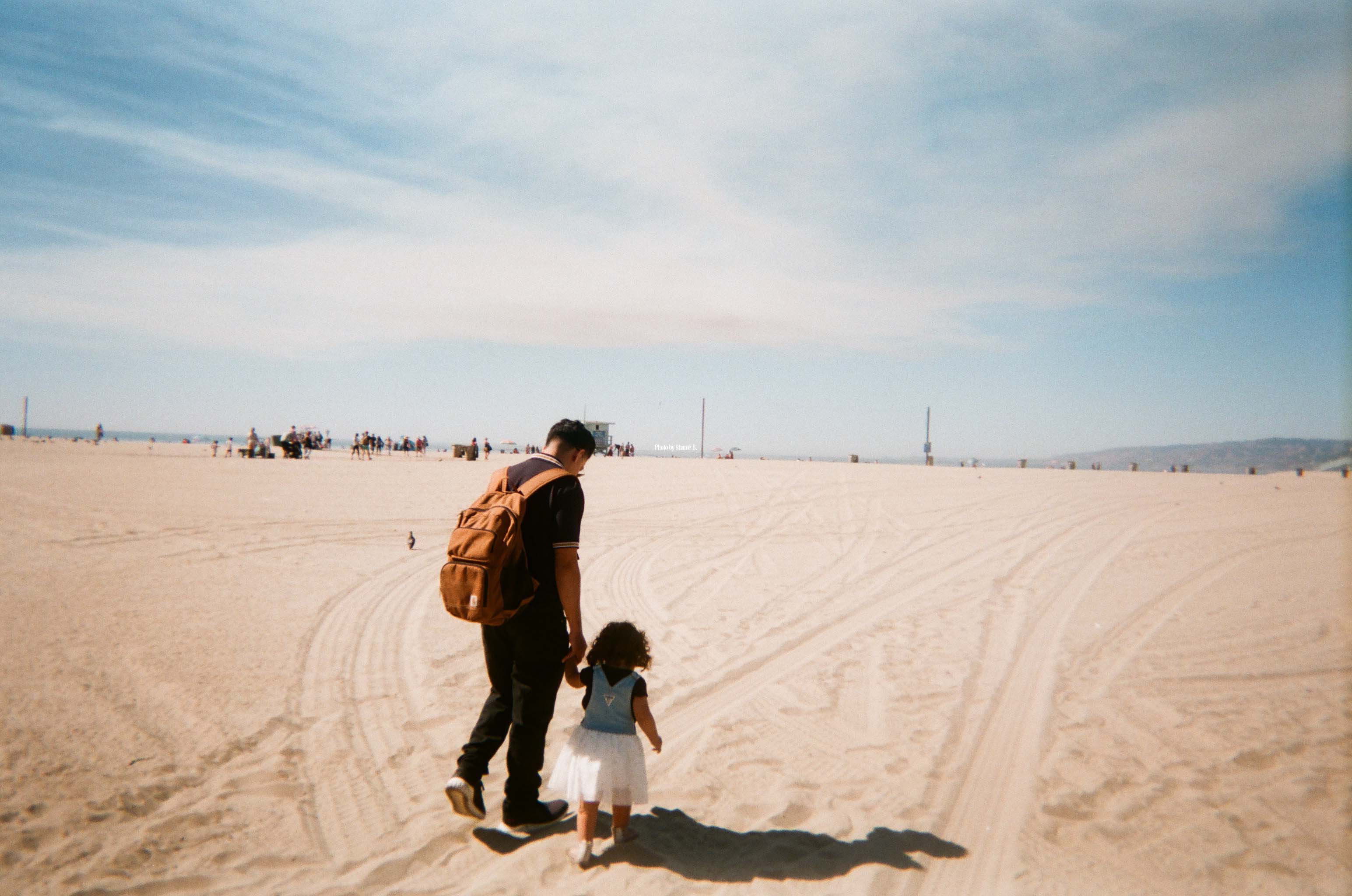 A picture of an adult and child walking on a beach.